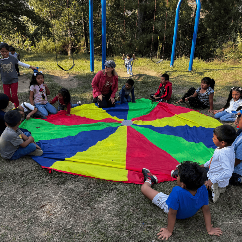 Volunteer with children sponsored by Be Humanitarian in Guatemala, sitting around a colourful parachute during activities.