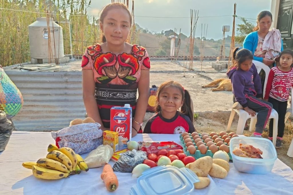 Two Guatemalan girls with fresh food supplies received through a fight malnutrition volunteer vacation Guatemala