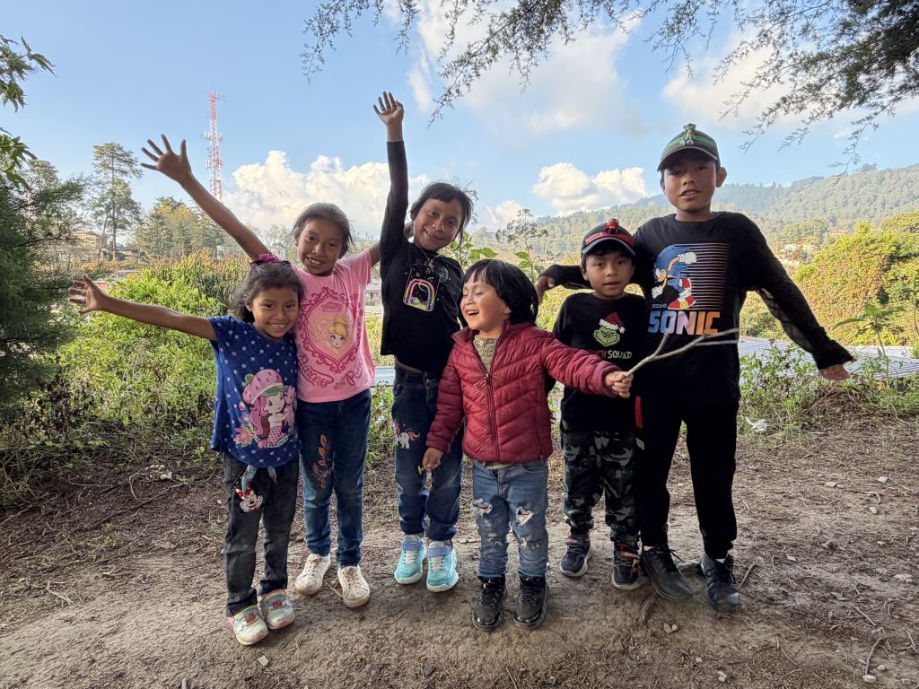 The impact of child sponsorship funding: smiling children with raised arms playing outdoors in a mountain village.